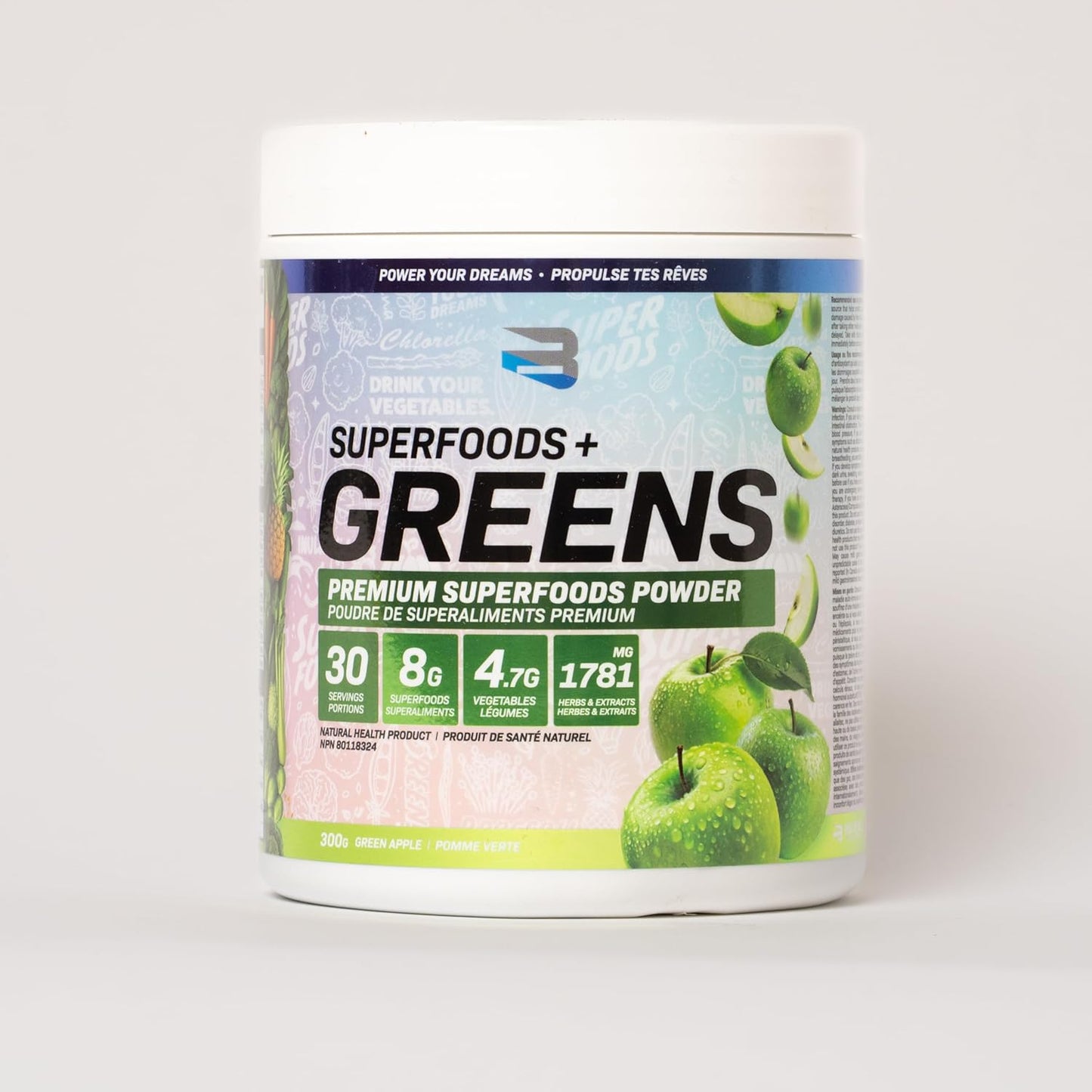Container of Superfoods + Greens powder with green apples on a white background