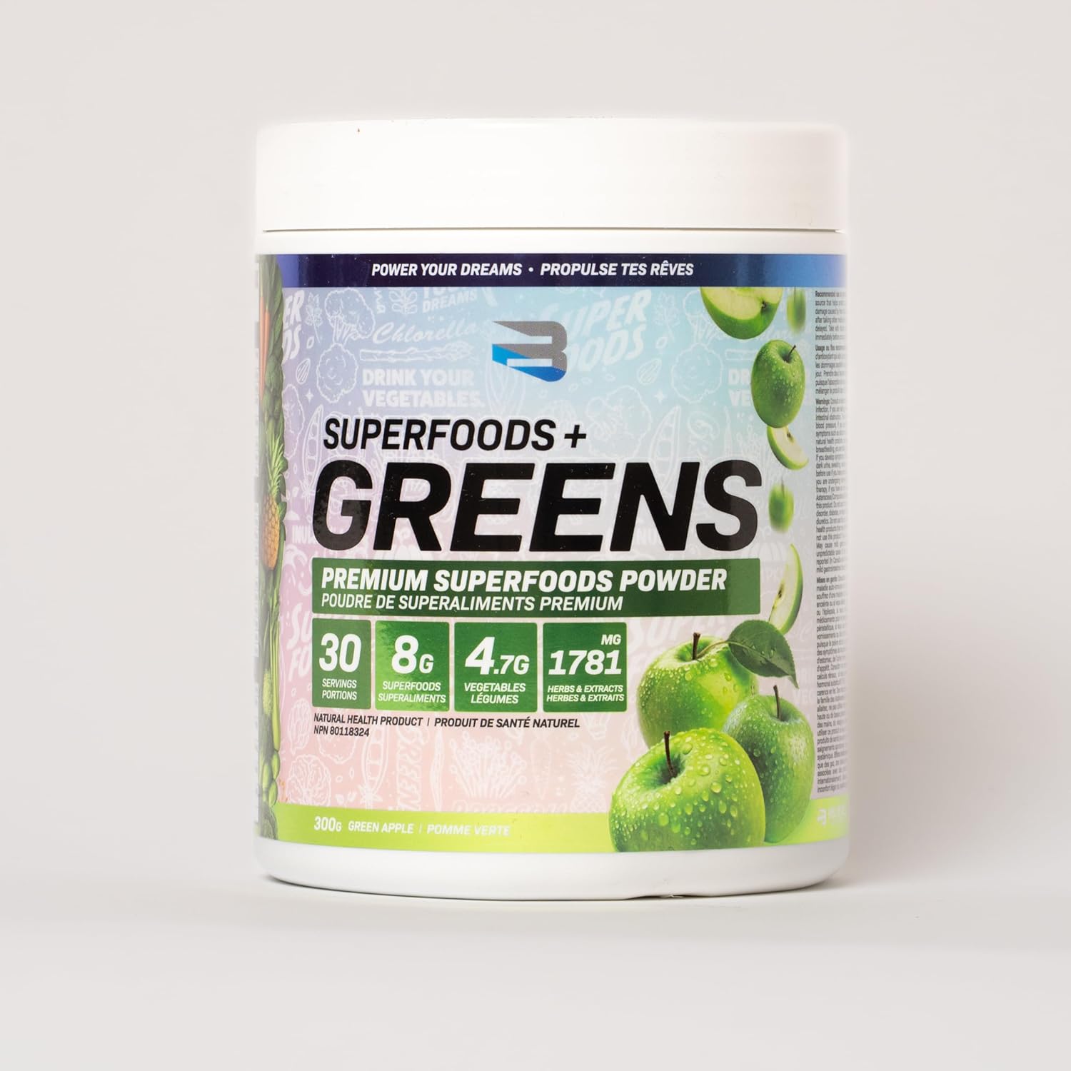 Container of Superfoods + Greens powder with green apples on a white background