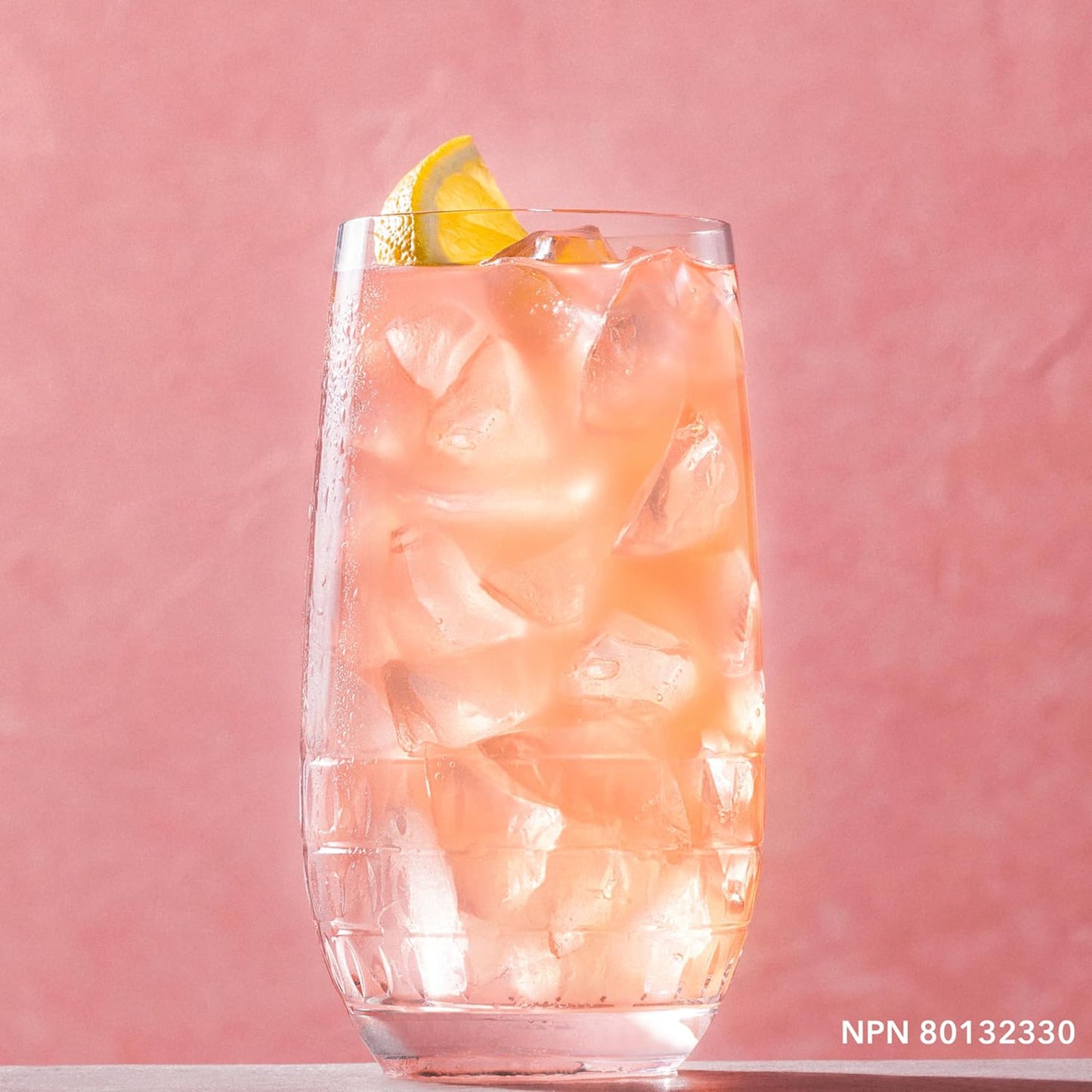 Glass of pink iced drink with a lemon wedge on a pink background