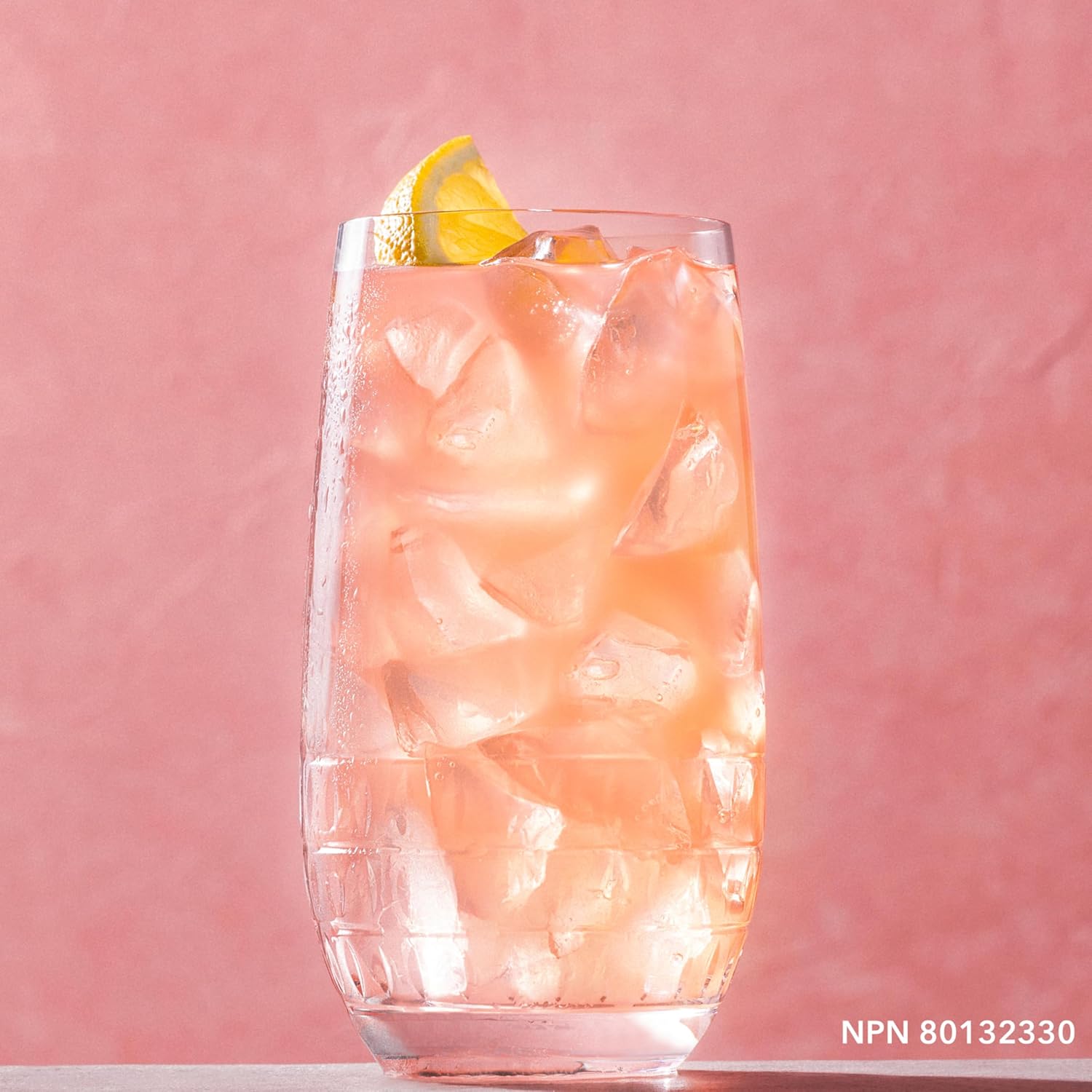 Glass of pink iced drink with a lemon wedge on a pink background