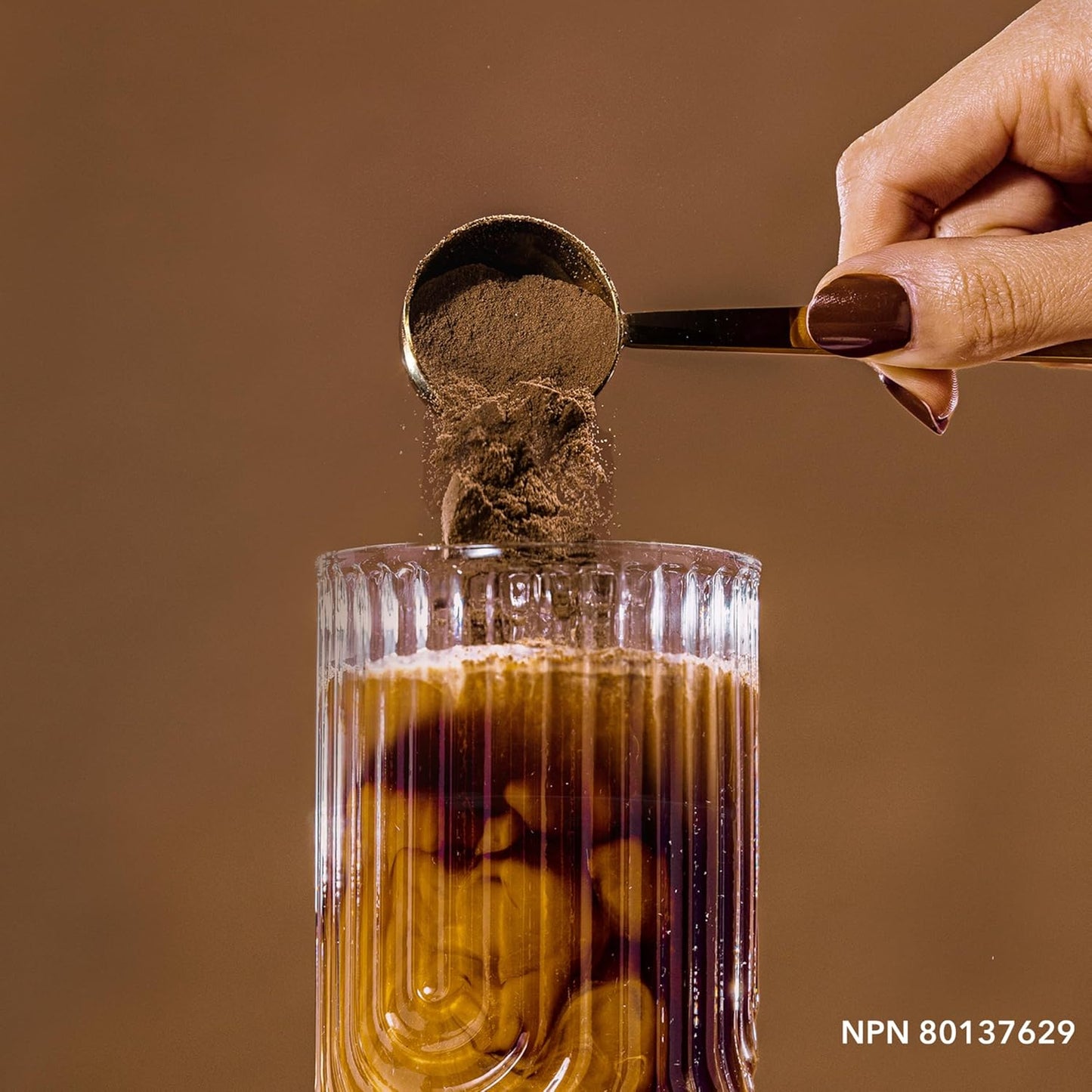 Spoon adding a brown powder to a glass of liquid on a brown background