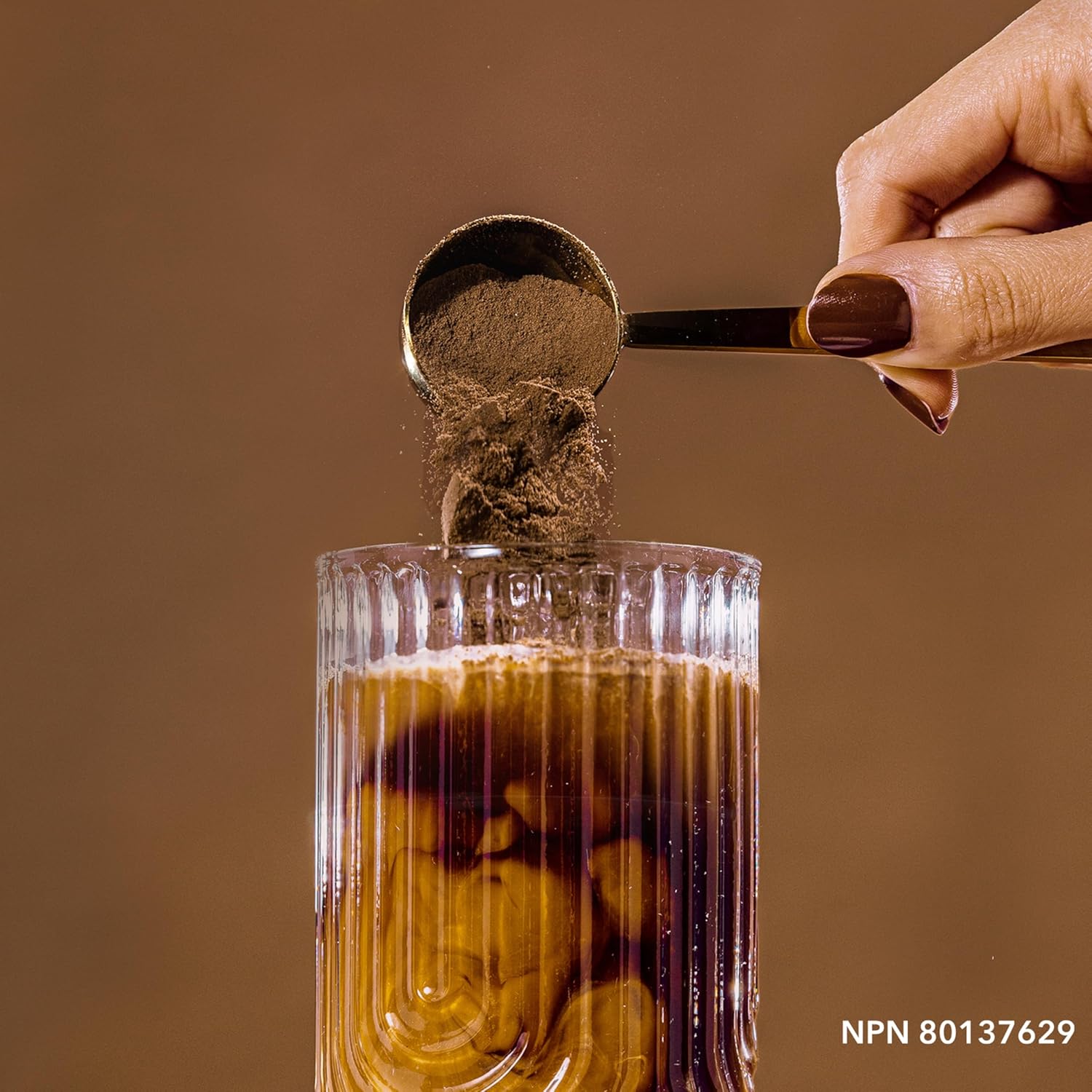 Spoon adding a brown powder to a glass of liquid on a brown background